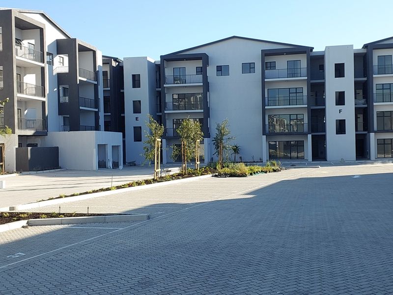 Modern multi-story residential apartment complex featuring paved parking areas, landscaped garden beds, and private balconies on each level.