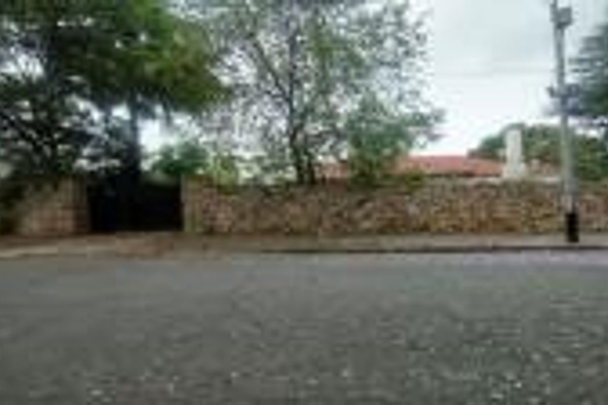 A street-level view of the property showing a stone boundary wall, gated entrance, and a glimpse of the tiled roof structure.