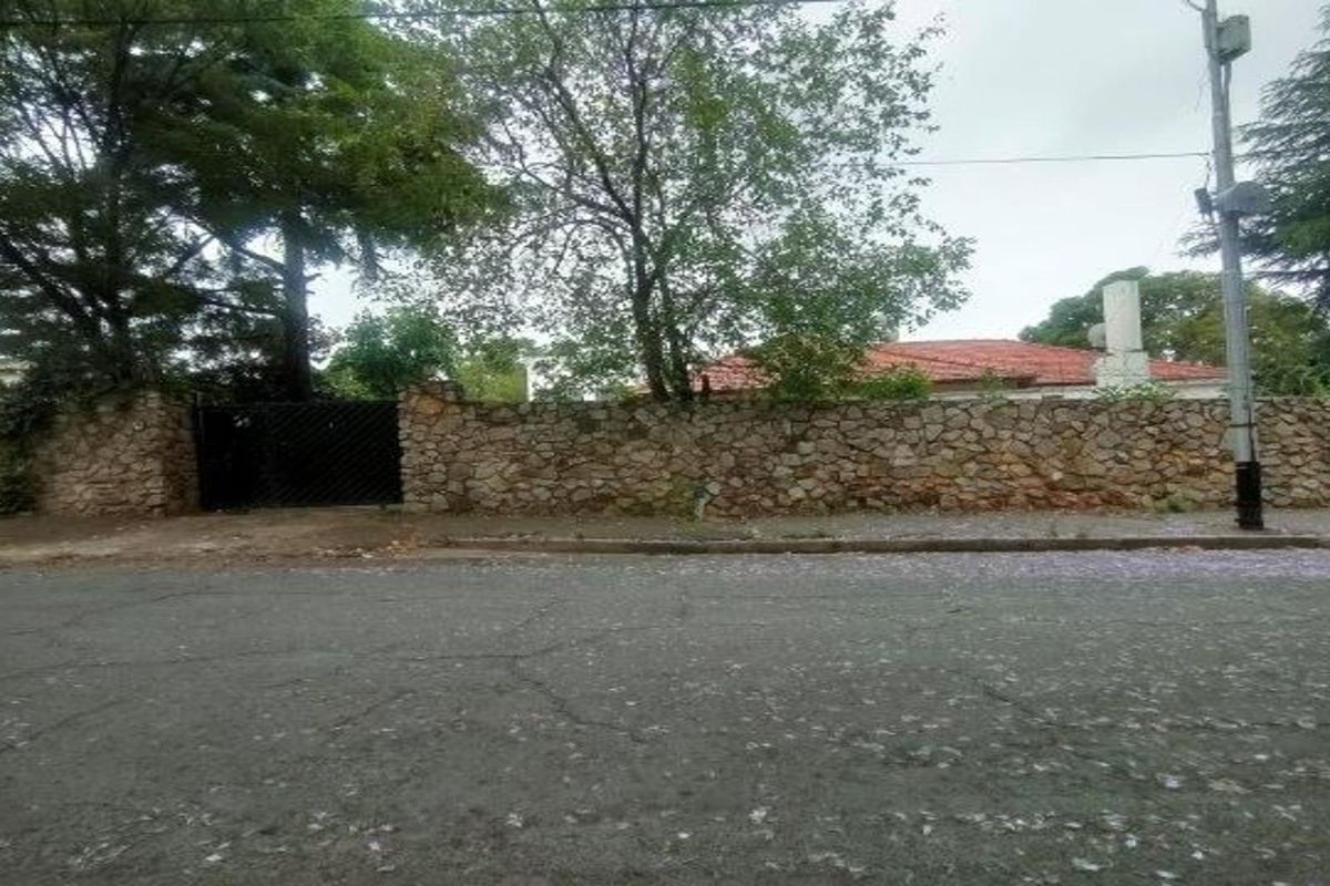 Street view of the property showing a stone boundary wall, metal gate, and a glimpse of the tiled roof behind mature trees.
