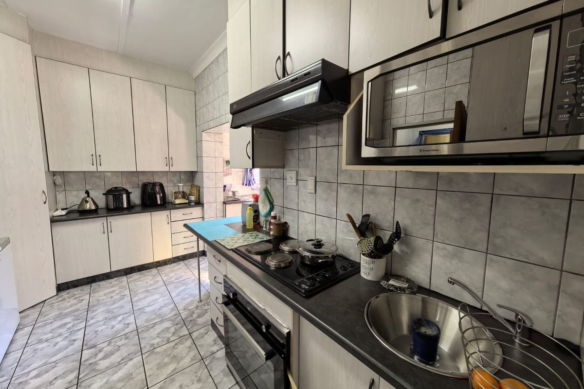 Functional kitchen featuring light-toned cabinetry, dark laminate countertops, tiled backsplash, and integrated appliances including an oven, hob, and microwave.
