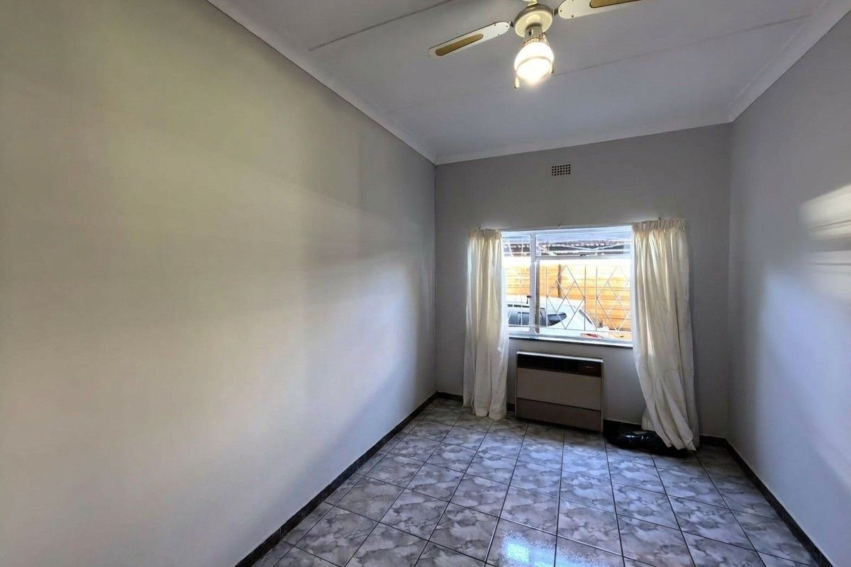A vacant bedroom featuring tiled flooring, a ceiling fan, and a built-in air conditioning unit with security bars on the window.