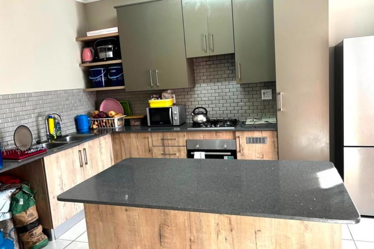 Modern kitchen featuring wood-look cabinetry, stone countertops, a central island, subway tile backsplash, and integrated gas hob with oven.