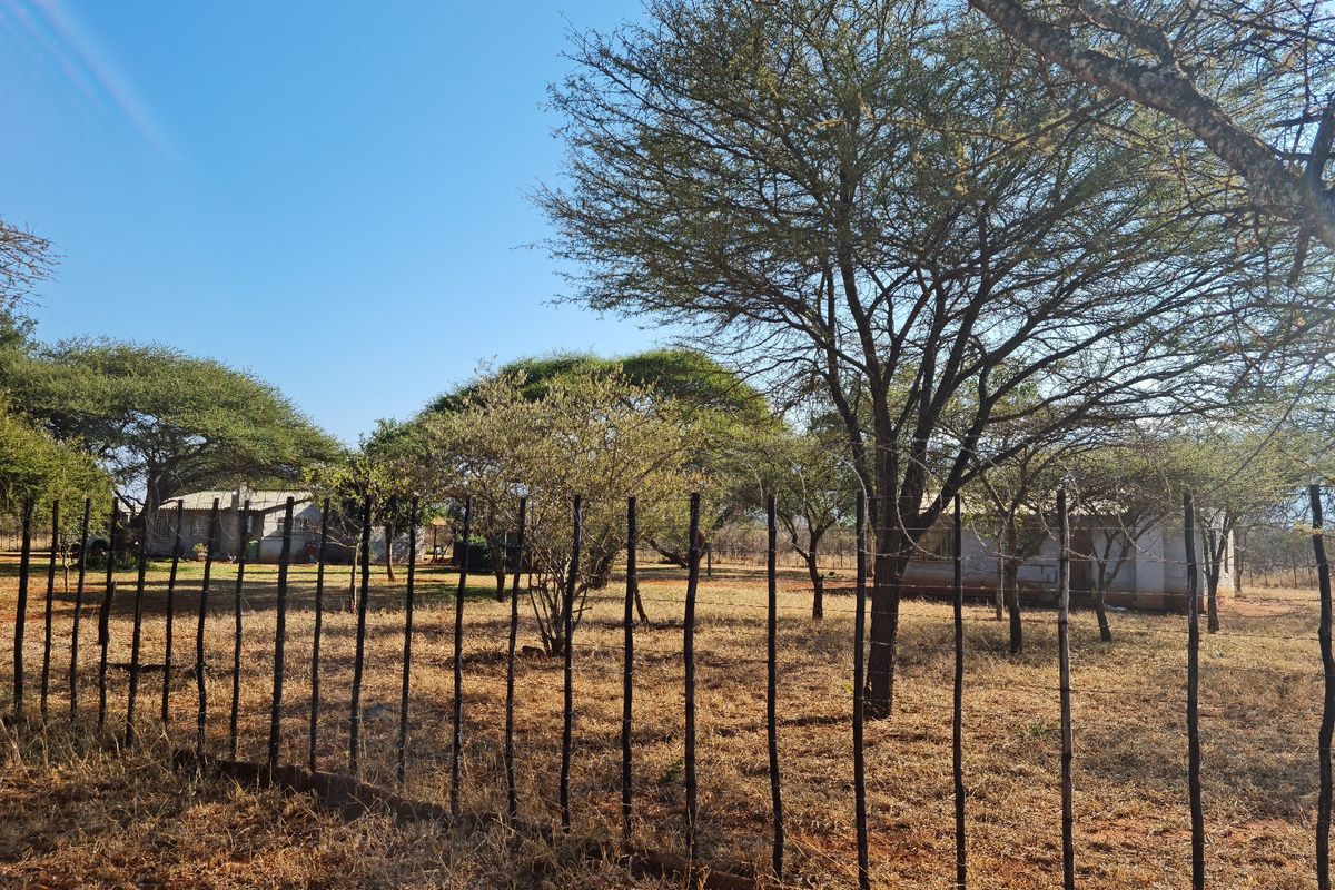 A view of the farm property grounds featuring mature trees and a wire perimeter fence with wooden posts.