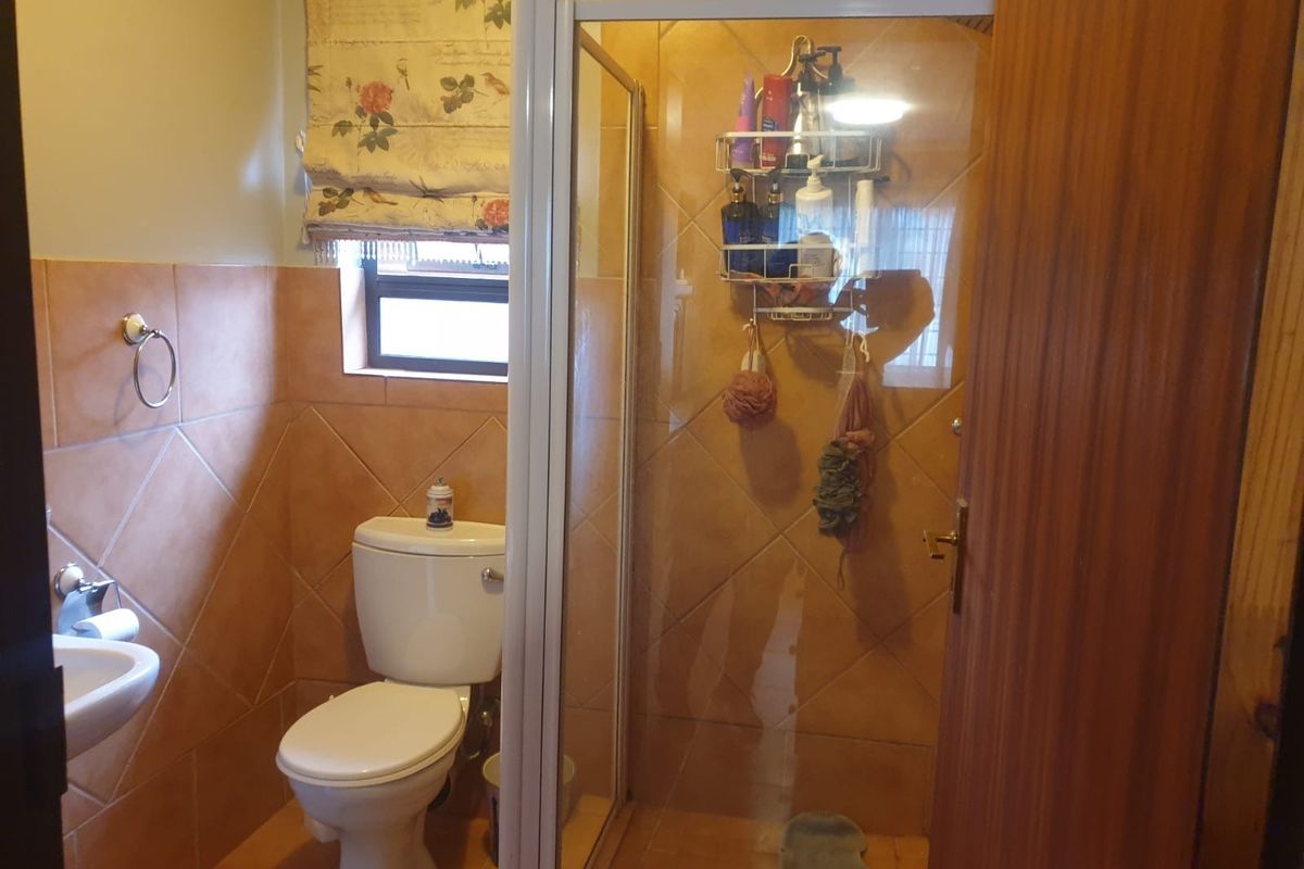 A functional bathroom featuring a shower enclosure, toilet, and washbasin with tiled walls and flooring.