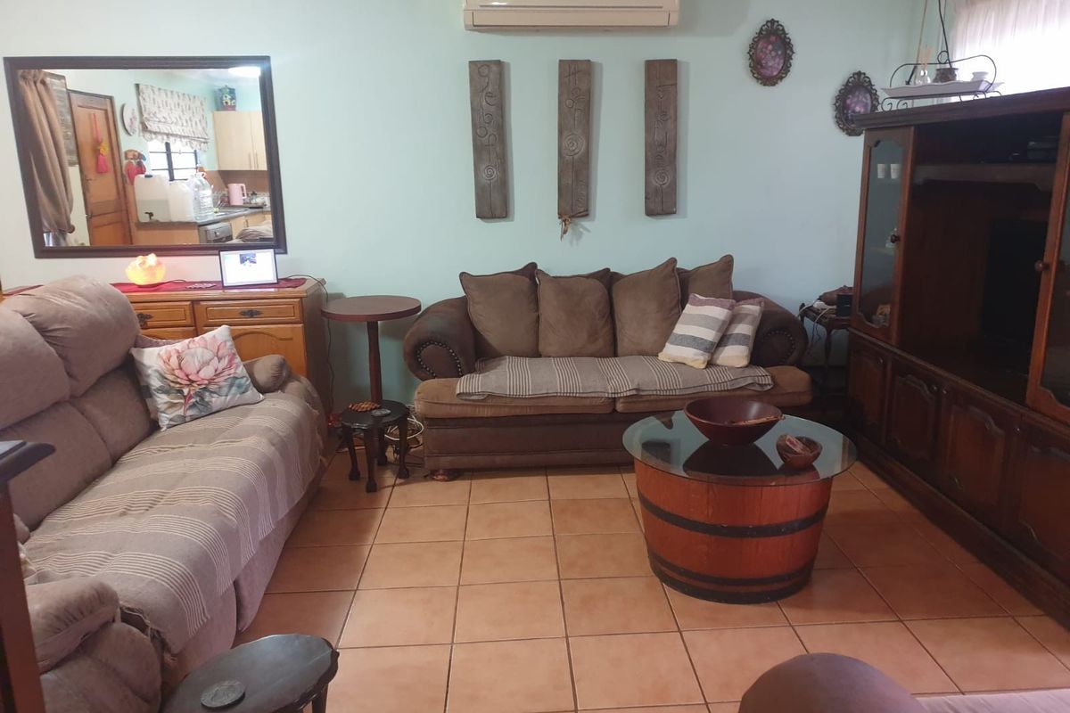 A comfortable living room featuring ceramic floor tiles, a wall-mounted air conditioning unit, and a ceiling fan.