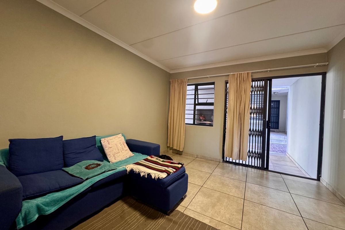 A living room featuring tiled flooring, a security gate leading to an outdoor area, and a louvre window, providing a functional and accessible living space.