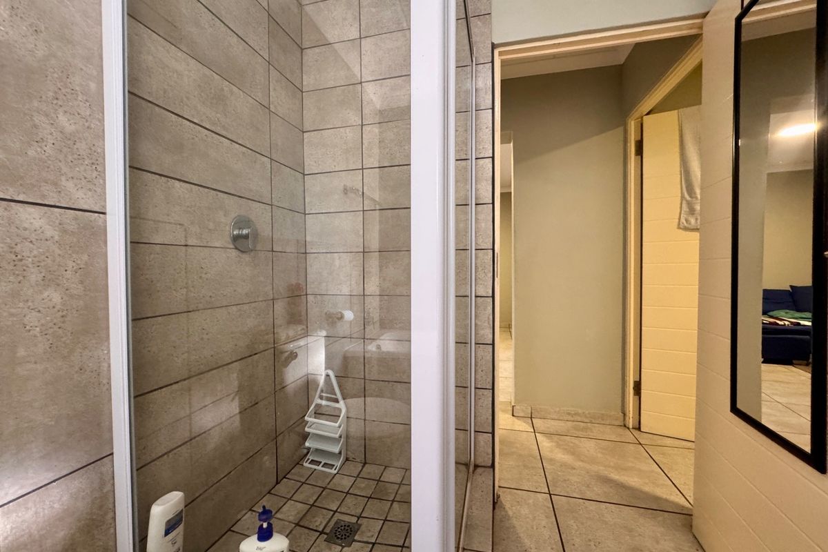 A functional bathroom featuring a tiled shower enclosure and neutral floor tiling, providing a clean and practical space.