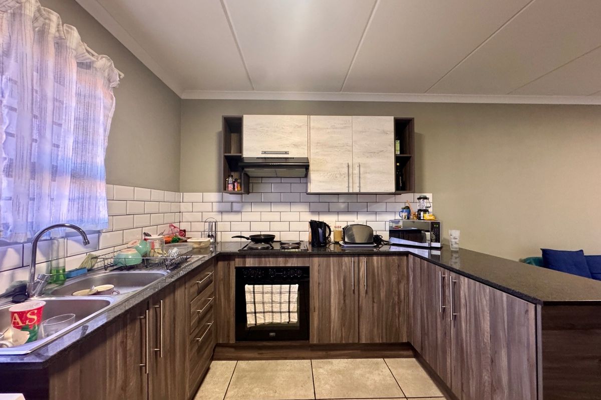 A functional kitchen featuring wood-look cabinetry, dark laminate countertops, a subway tile backsplash, and integrated cooking appliances including an oven and hob.