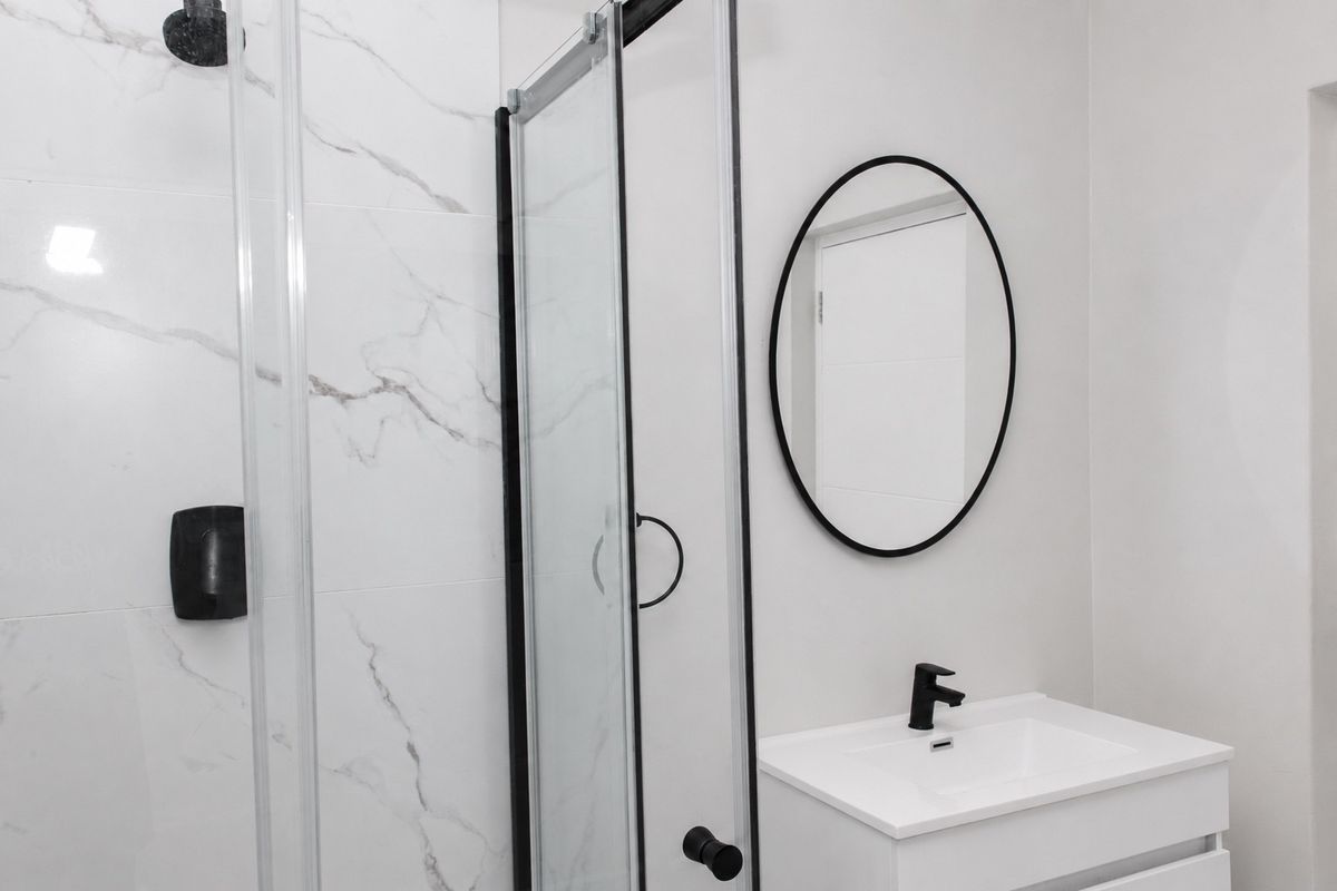 Modern bathroom featuring a glass shower enclosure with marble-look wall tiles, a vanity basin with black tapware, and a matching black-framed mirror.