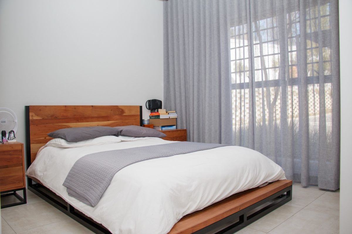 A well-maintained bedroom featuring neutral tiled flooring and floor-to-ceiling curtains, providing a clean and simple aesthetic.