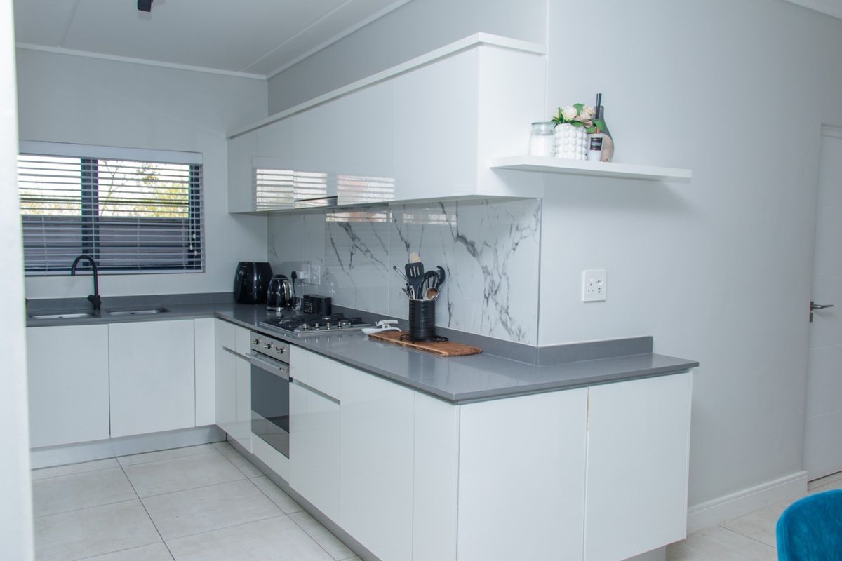 Modern kitchen featuring sleek white cabinetry, stone countertops, a marble-look splashback, and integrated stainless steel appliances.