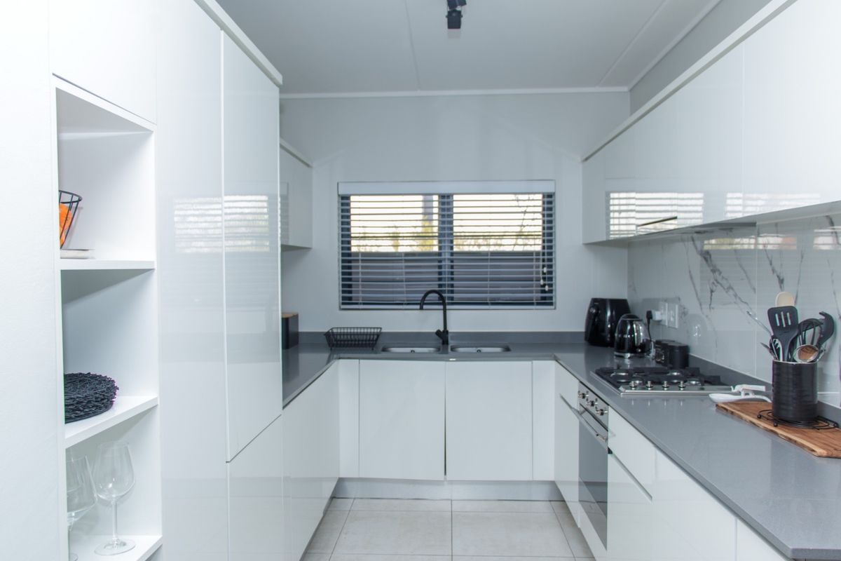 Modern U-shaped kitchen featuring high-gloss white cabinetry, stone countertops, marble-look splashback, and integrated stainless steel appliances.