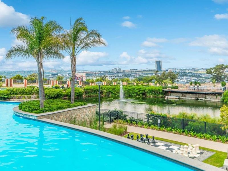 A well-maintained swimming pool area featuring a stone-clad retaining wall, water fountain, and landscaped garden with expansive views of the surrounding landscape.