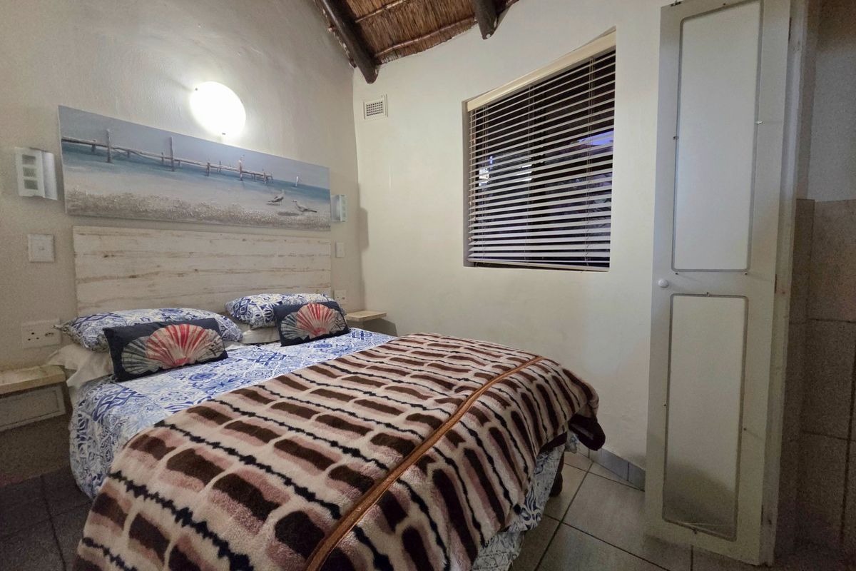 A cozy bedroom featuring a vaulted thatch ceiling with exposed timber beams, tiled flooring, and a built-in cupboard.