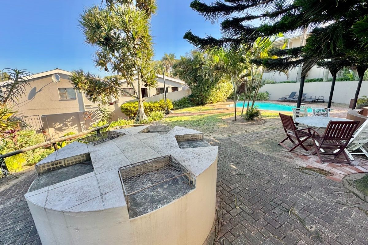 Outdoor entertainment area featuring a swimming pool, paved patio, and a large circular built-in braai facility set within a landscaped garden.