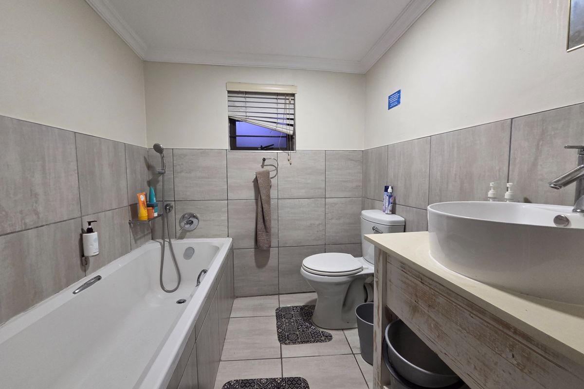 A functional bathroom featuring a bathtub with shower mixer, a vessel sink on a vanity, and neutral wall and floor tiling.