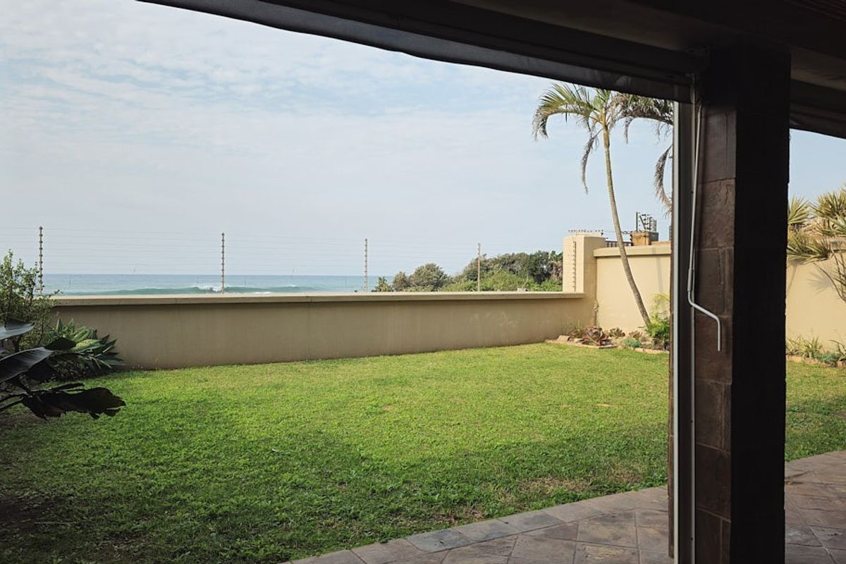 A private rear garden featuring a well-maintained lawn, paved patio area, and boundary wall with electric fencing, offering direct ocean views.