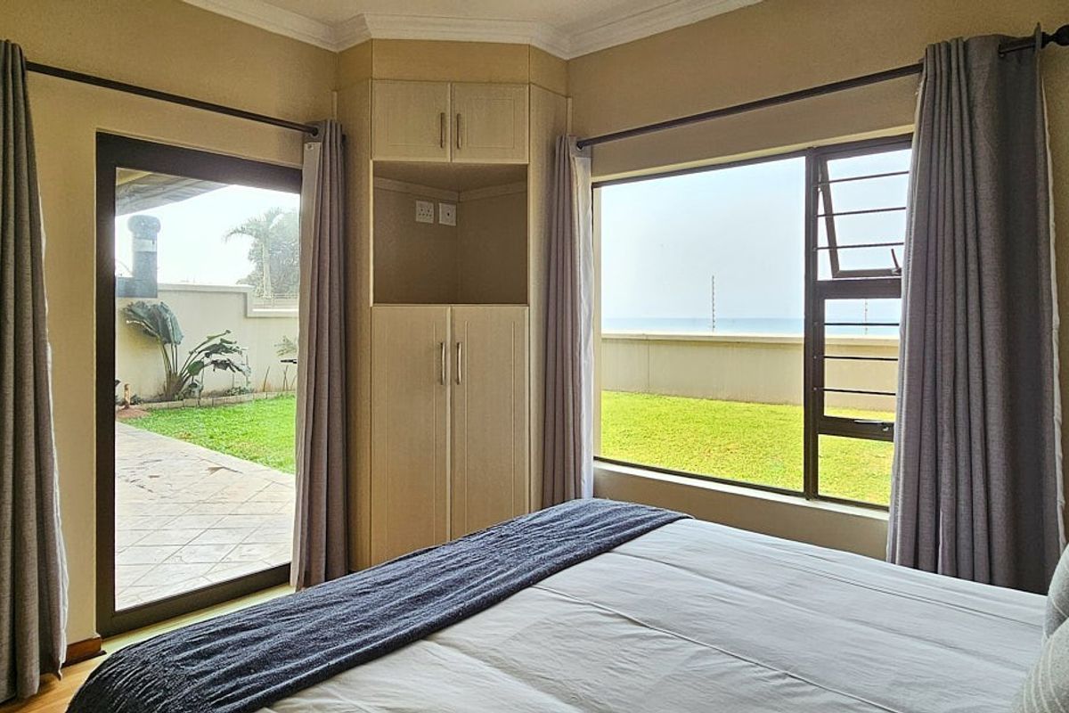 A bright bedroom featuring a built-in corner cupboard, large aluminium windows, and a sliding door providing direct access to the garden area.