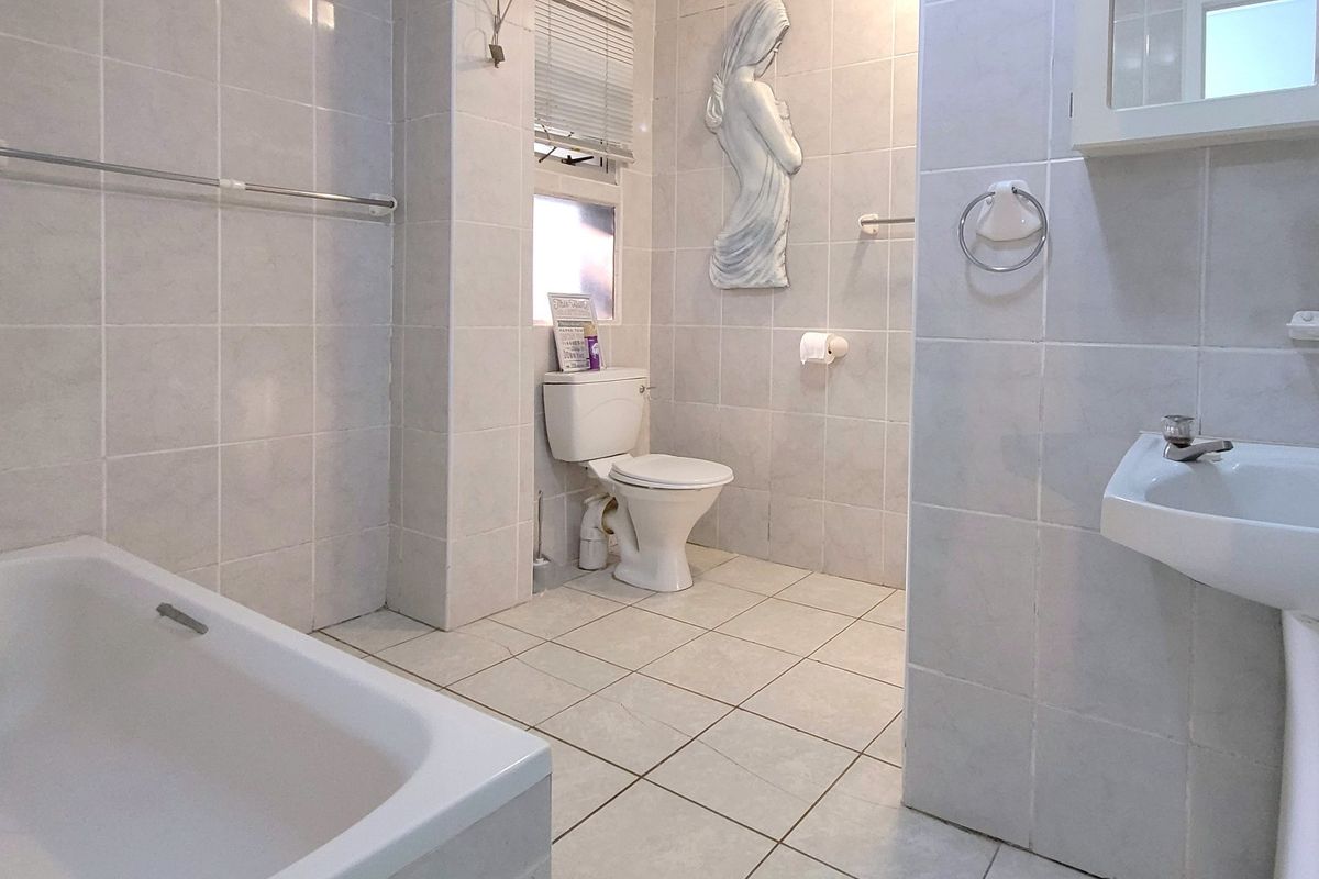 A functional bathroom featuring a bathtub, pedestal sink, and toilet, finished with neutral ceramic wall and floor tiles.