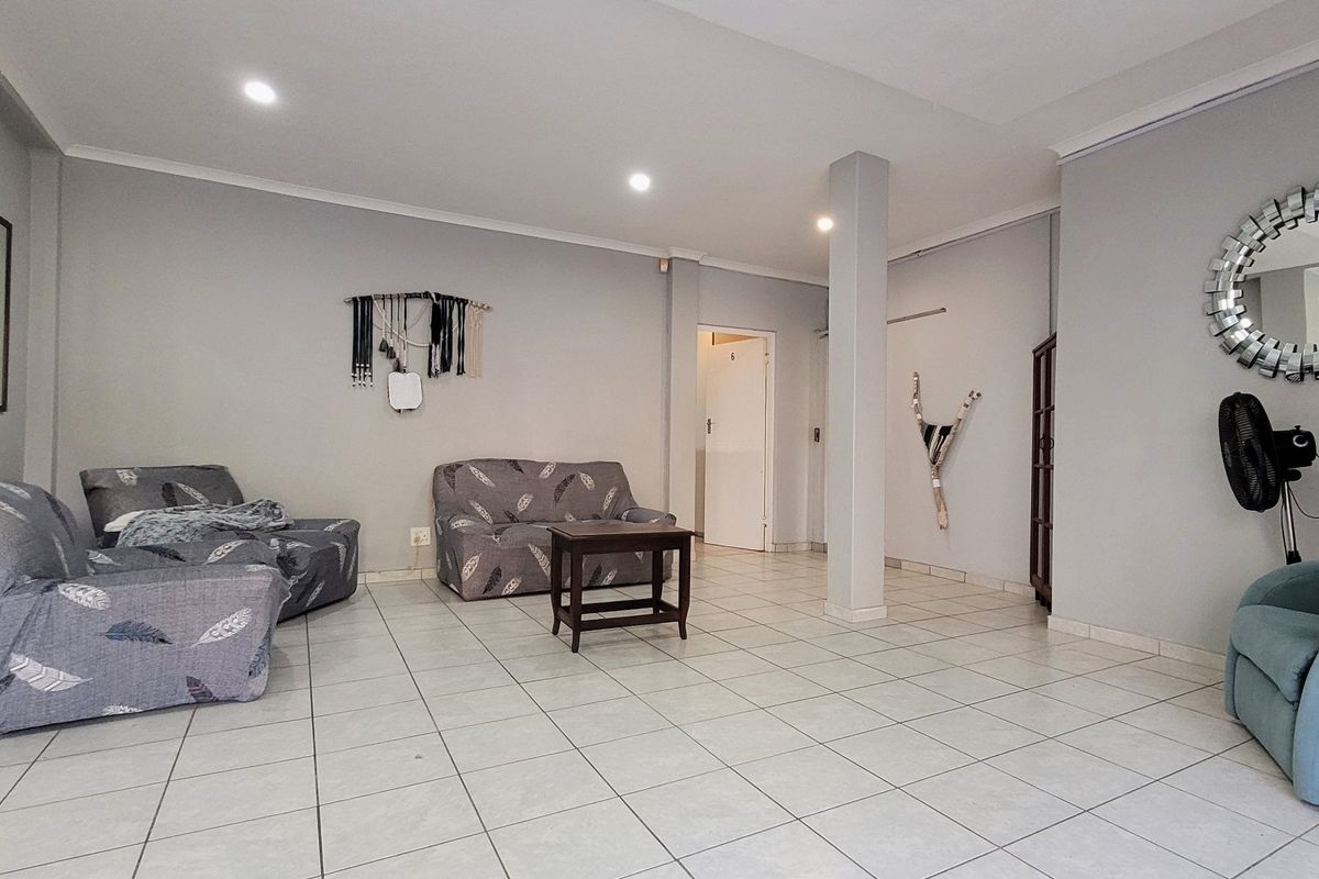 Spacious living area featuring neutral grey walls, ceramic floor tiles, and recessed downlighting, providing a versatile open-plan layout.