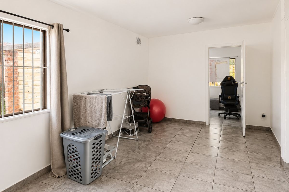A neutral bedroom featuring tiled flooring, a window with security bars, and a doorway leading to an adjacent room.