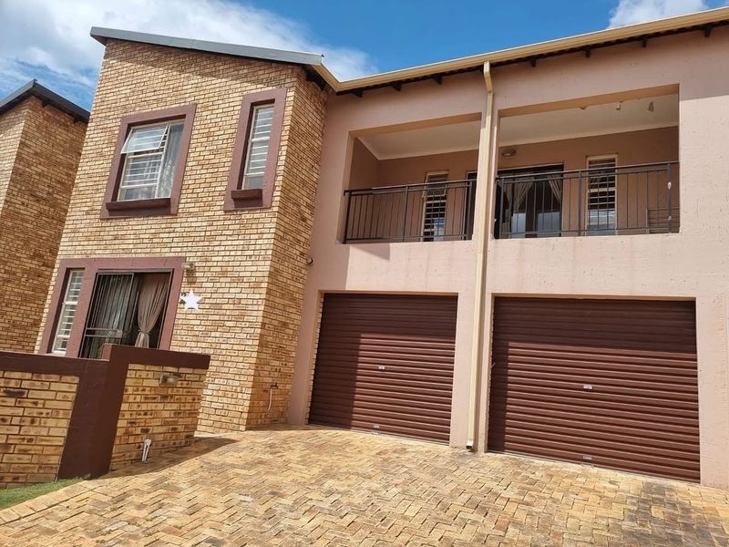 Front view of a double-story residential property featuring a double garage with roller shutter doors and an upper-level balcony with metal railings.