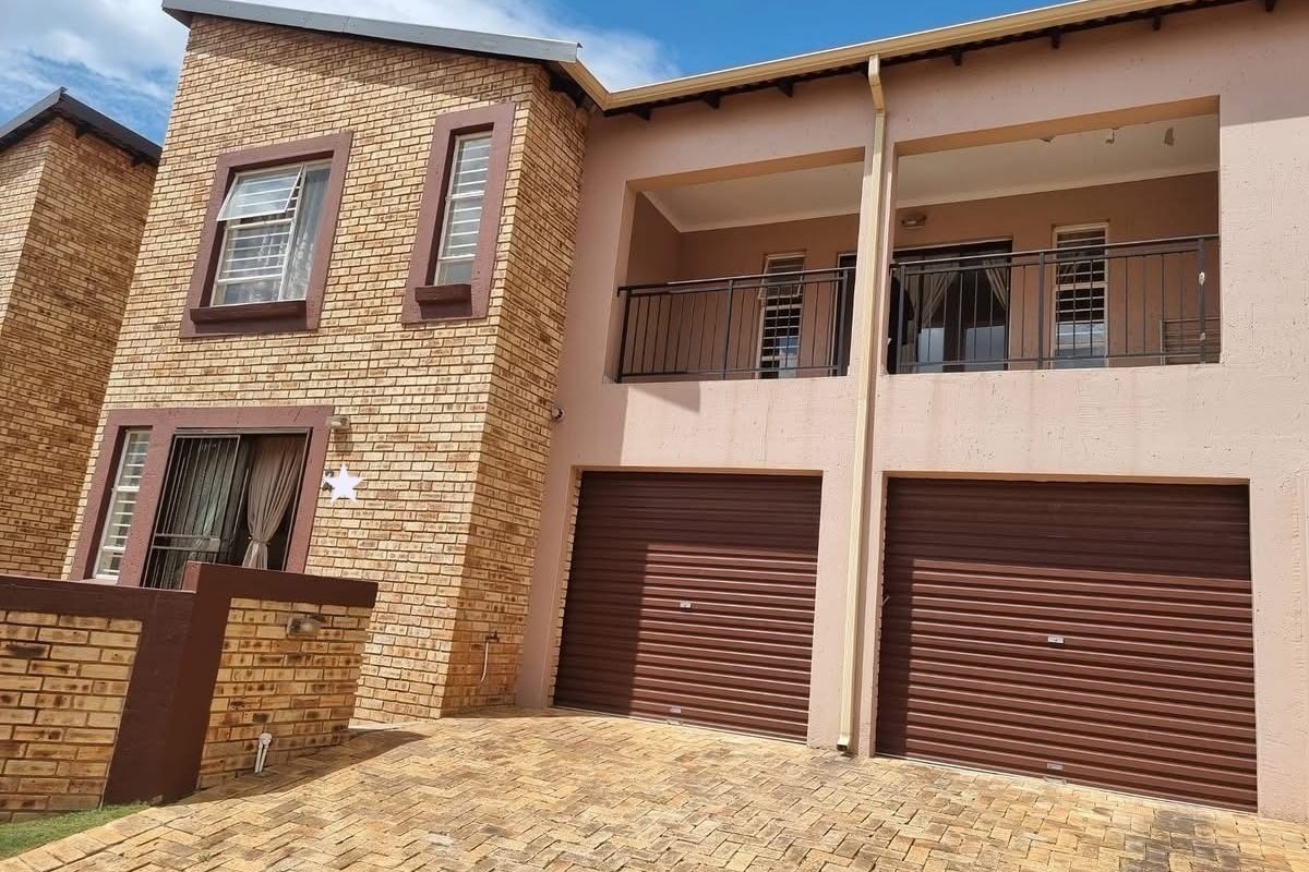 Front view of a double-story residential property featuring a double garage with roller shutter doors and an upper-level balcony with metal railings.