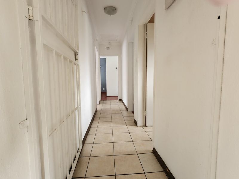 A functional, tiled hallway providing access to multiple rooms, featuring a built-in security gate and neutral wall finishes.