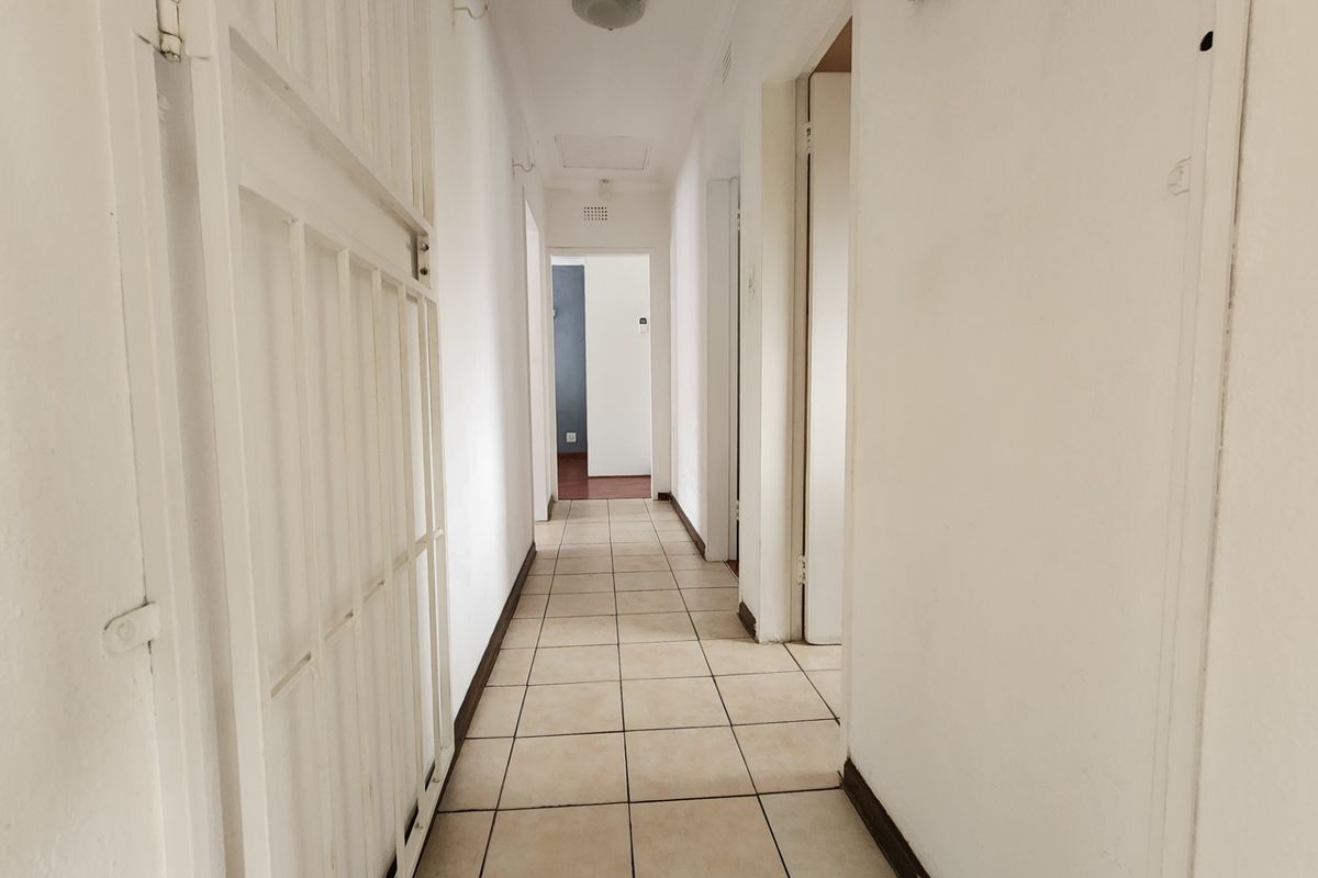 A functional, tiled hallway providing access to multiple rooms, featuring a built-in security gate and neutral wall finishes.