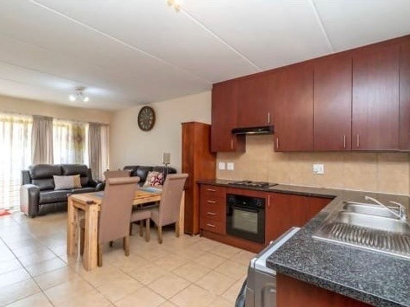 Open-plan living and kitchen area featuring dark wood cabinetry, granite countertops, integrated oven, and tiled flooring throughout.