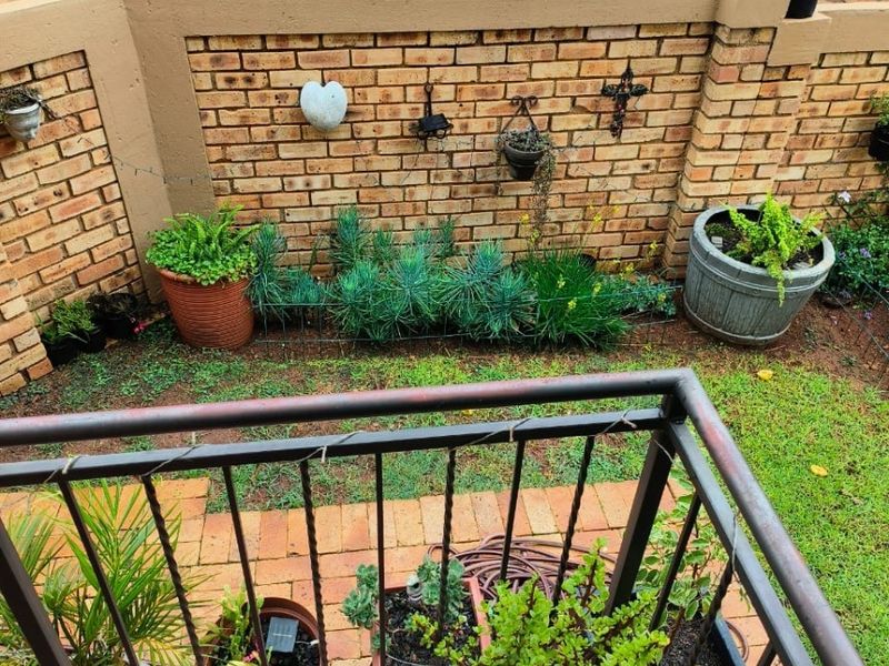 A small outdoor balcony area featuring brick boundary walls, tiled flooring, and a metal safety railing overlooking a paved driveway.