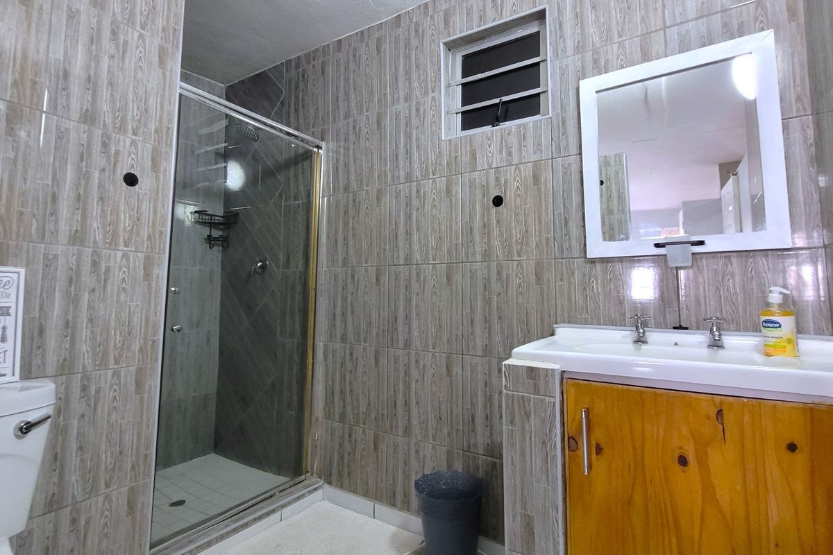 A functional bathroom featuring full-height wood-look ceramic wall tiles, a glass shower enclosure, and a wooden vanity cabinet with a basin.