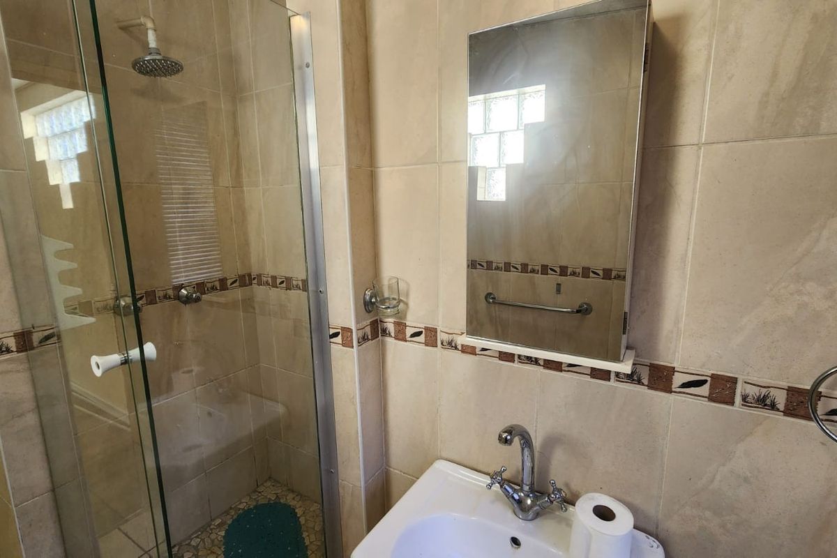 A functional bathroom featuring a glass-enclosed shower, pedestal sink, and wall-mounted medicine cabinet with neutral tiled walls and a glass block window.