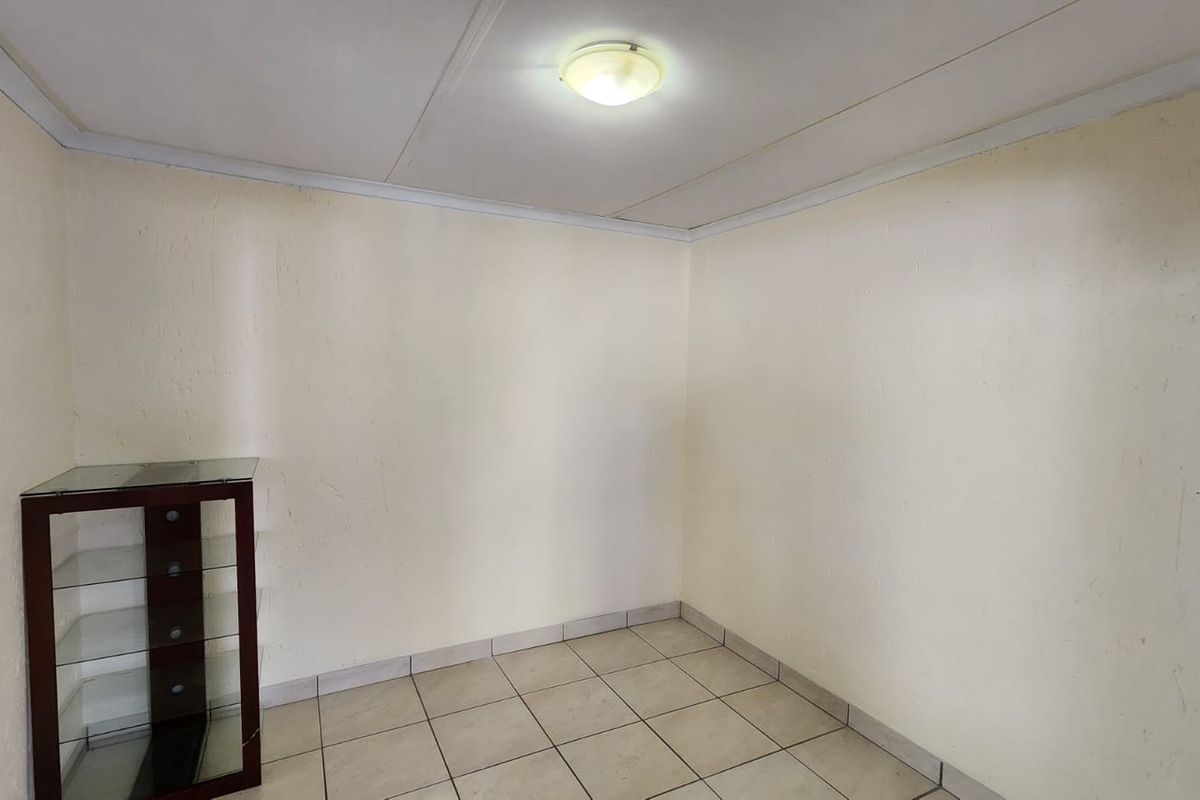 A simple, empty bedroom featuring tiled flooring and neutral walls, offering a blank canvas for potential interior design updates.