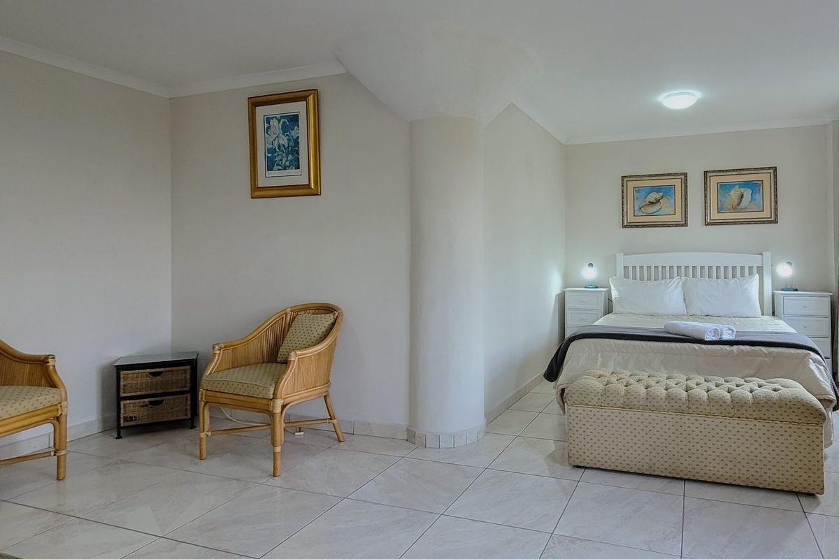 A spacious bedroom featuring neutral tiled flooring, a central structural column, and ample natural light, providing a clean and functional living space.