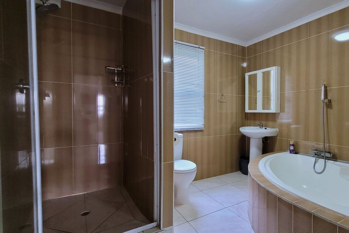 A functional bathroom featuring a walk-in shower, a built-in bathtub, a pedestal basin, and full-height wall tiling.