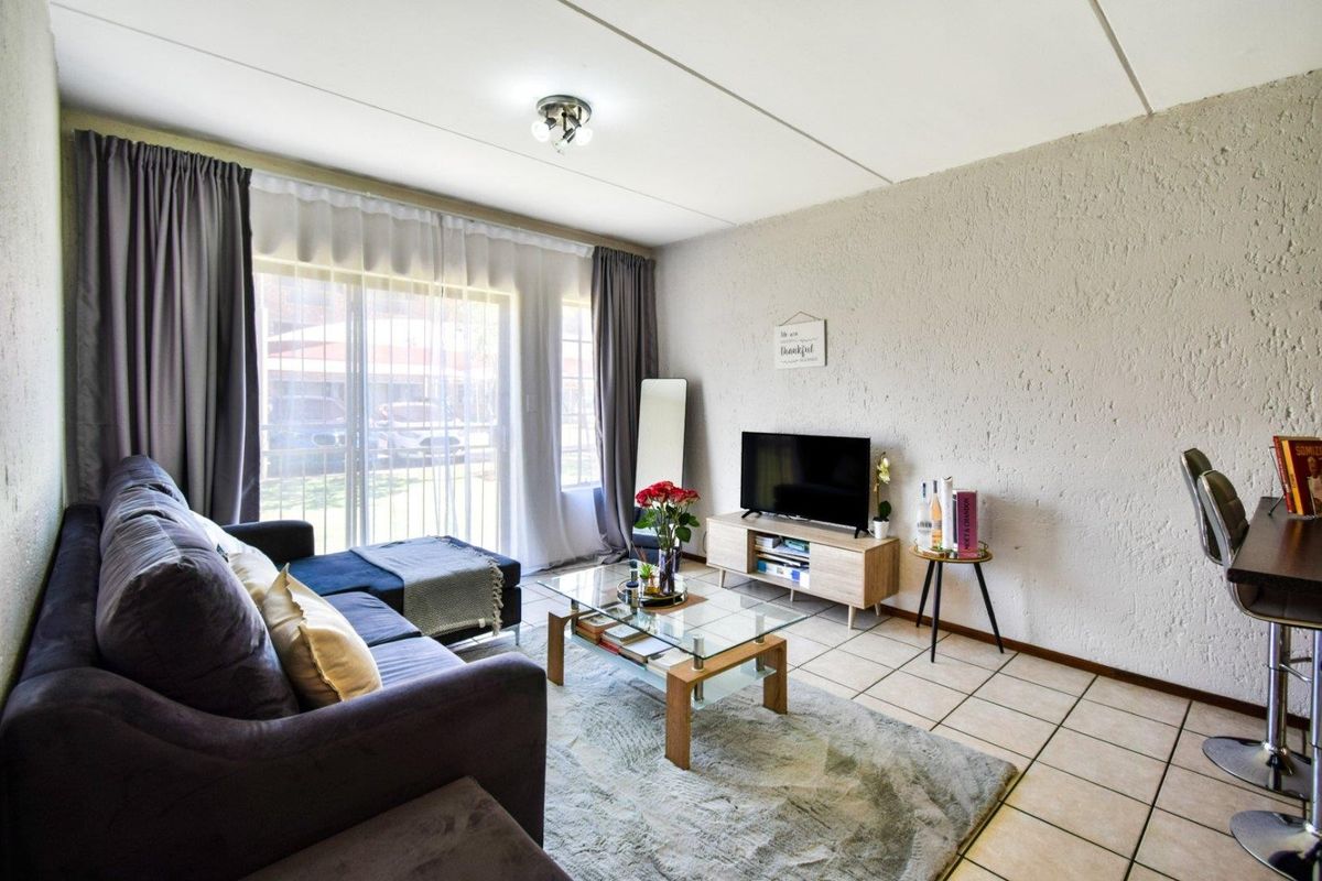 A bright living room featuring tiled flooring, textured walls, and a large sliding glass door providing access to the exterior.