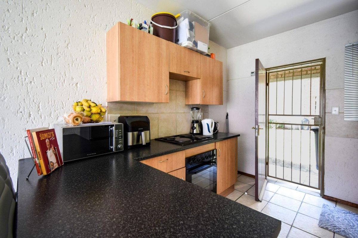 Compact kitchen featuring laminate cabinetry, dark countertops, built-in oven and hob, with direct access to an exterior security gate.