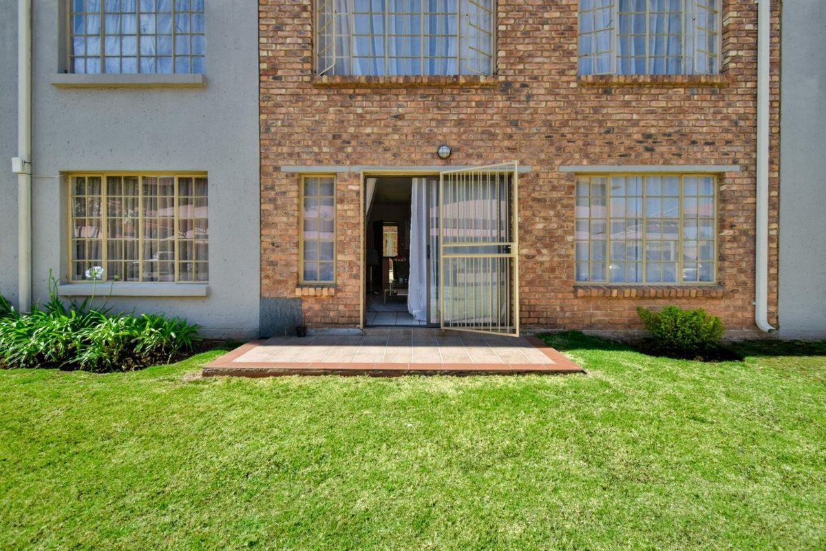 Rear view of the apartment featuring a face brick facade, a small tiled patio area, and access to a private lawn.