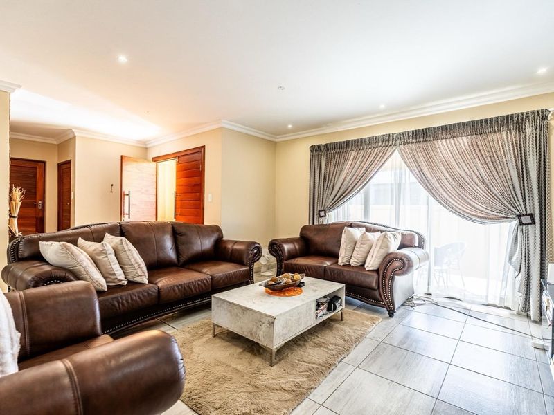 A well-lit living room featuring tiled flooring, recessed downlights, and a sliding glass door providing access to the outdoor area.