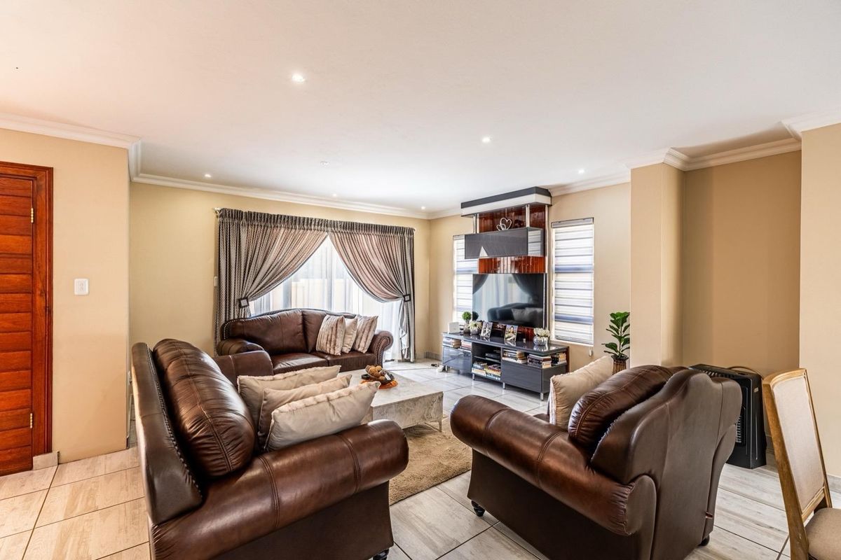 A well-maintained living room featuring tiled flooring, recessed downlighting, decorative cornice, and a custom built-in media unit.