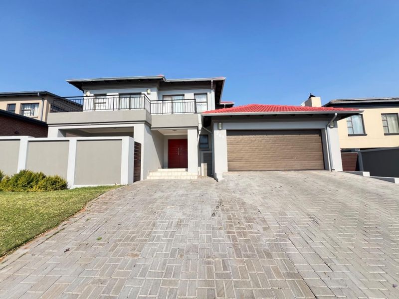 Front elevation of a modern double-story house featuring a paved driveway, double garage, and an upper-level balcony.