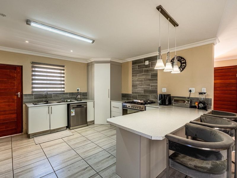 Modern kitchen featuring a central island, gas hob, built-in oven, integrated dishwasher, and stone countertops with contemporary tiled flooring.