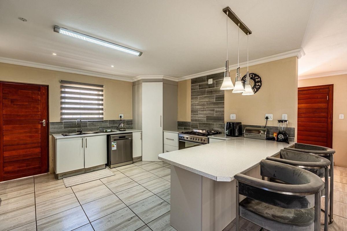 Modern kitchen featuring a central island, gas hob, built-in oven, integrated dishwasher, and stone countertops with contemporary tiled flooring.