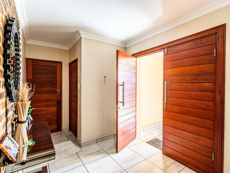 A bright and welcoming entrance hall featuring tiled flooring, crown molding, and distinctive solid timber doors with an exposed brick feature wall.