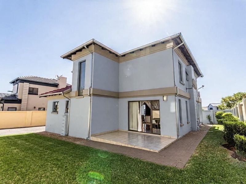Rear view of a two-story residential property featuring a tiled patio, sliding glass doors, and a well-maintained garden with boundary walls.