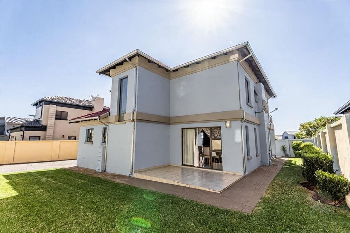 Rear view of a two-story residential property featuring a tiled patio, sliding glass doors, and a well-maintained garden with boundary walls.