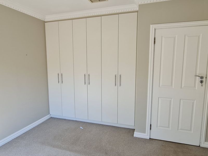 A clean, empty bedroom featuring neutral walls, carpet flooring, and a large built-in wardrobe with modern handles.