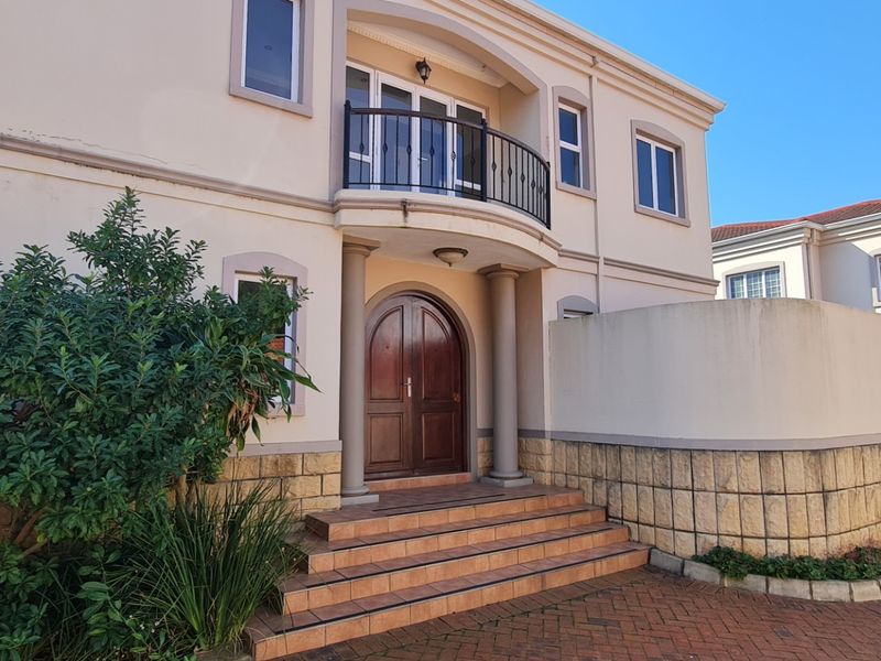 Front elevation of a townhouse featuring an arched wooden entrance door, a small balcony with wrought iron railing, and stone cladding accents.