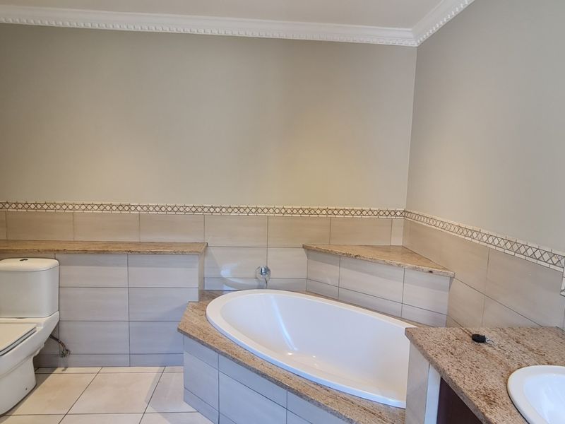 A clean, well-maintained bathroom featuring a built-in bathtub, granite vanity surfaces, neutral ceramic tiling, and a large wall-mounted mirror.